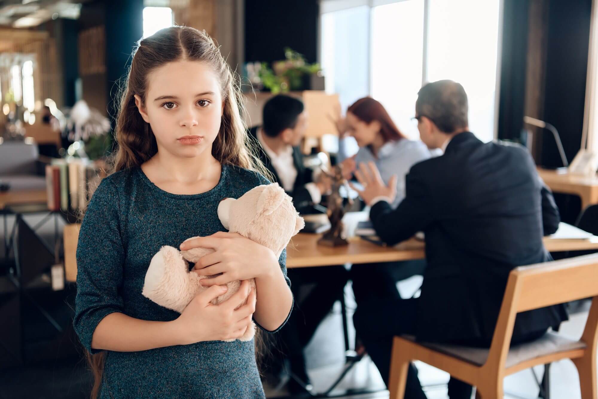 Girl holding teddy bear in office setting.
